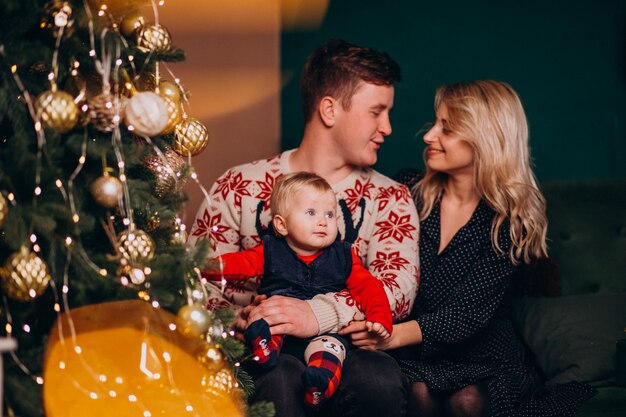 Familia joven con niña sentada junto a árbol de Navidad