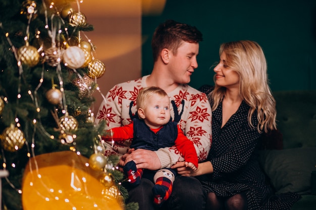 Familia joven con niña sentada junto a árbol de Navidad