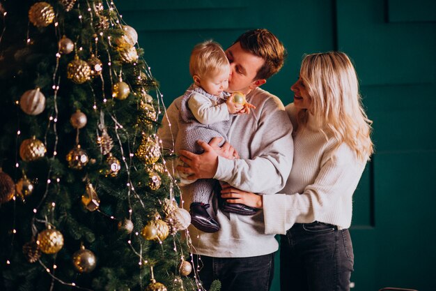 Familia joven con pequeña hija colgando juguetes en el árbol de Navidad