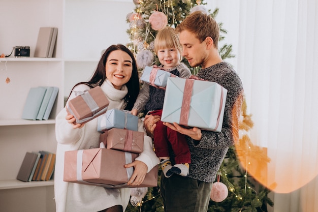 Familia joven con pequeño hijo por árbol de Navidad con regalos de Navidad