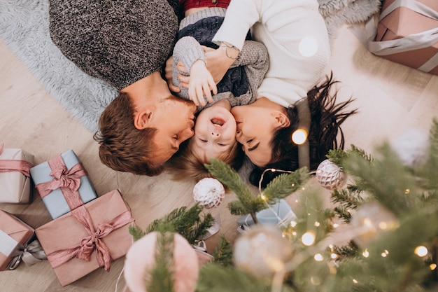 Familia joven con pequeño hijo bajo el árbol de Navidad