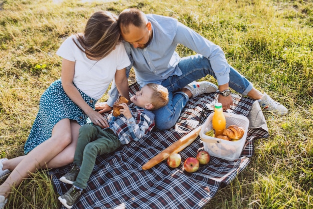 Familia joven con pequeño hijo haciendo picnic en el parque