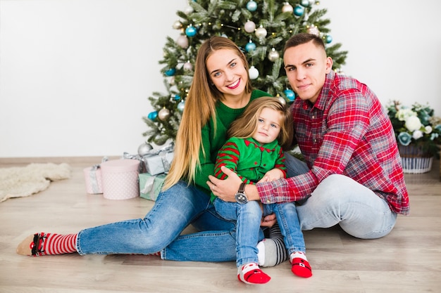 Familia joven sentados enfrente de árbol de navidad