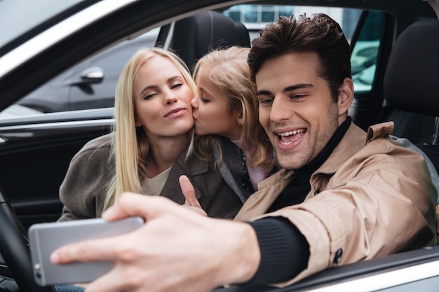 La familia joven sonriente hace selfie por teléfono móvil.