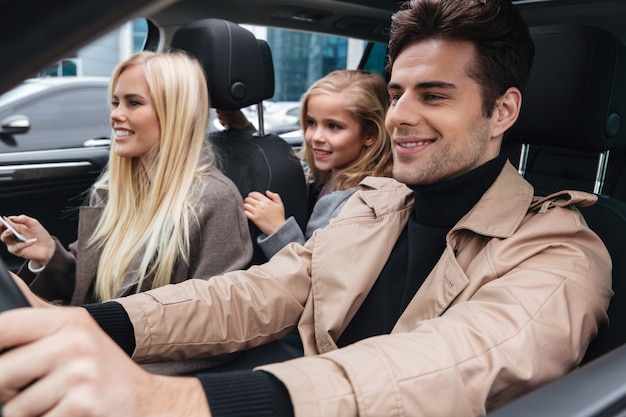 Familia joven sonriente que se sienta en coche