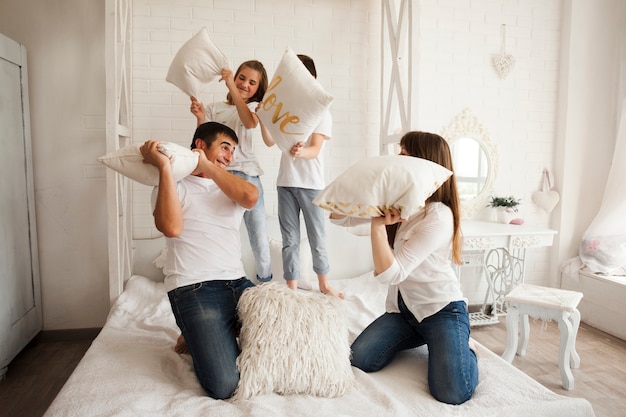 Familia juguetona teniendo pelea de almohadas graciosa en la cama