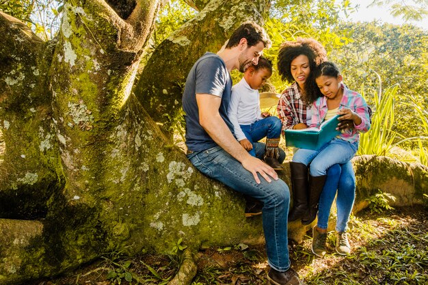 Familia leyendo juntos en un tronco de árbol