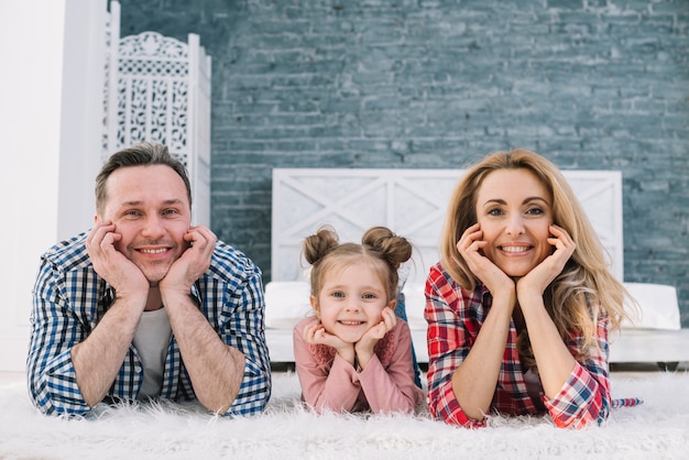 Foto gratuita familia linda alegre que miente en la alfombra que mira la cámara
