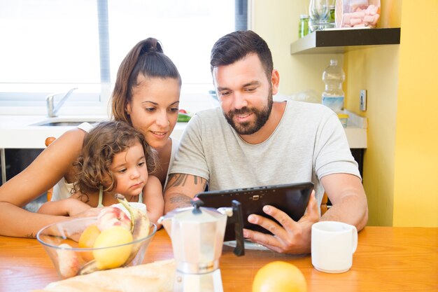 Familia mirando la pantalla de la tableta digital durante el desayuno