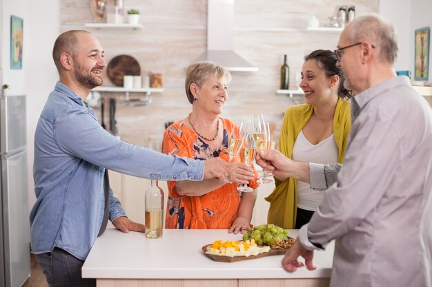 Familia multigeneracional tintineo de vasos con vino en la cocina de casa durante la reunión.