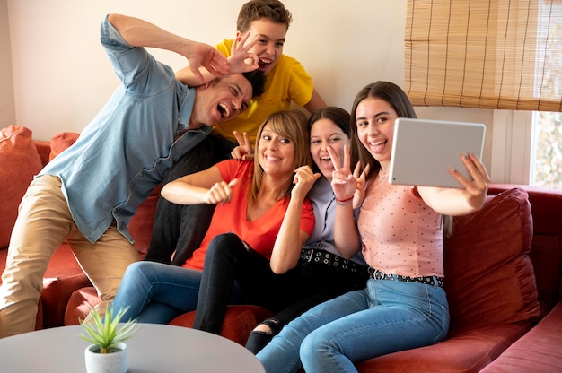 Familia con padres y tomando selfie con tableta en el sofá juntos