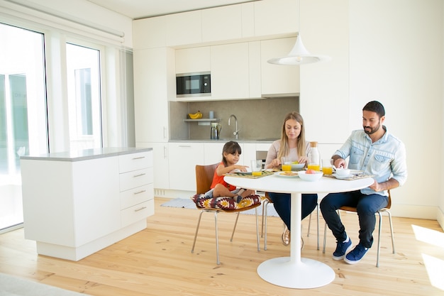 Familia pareja y niño desayunando juntos en la cocina, sentados en la mesa de comedor con plato y jugo de naranja