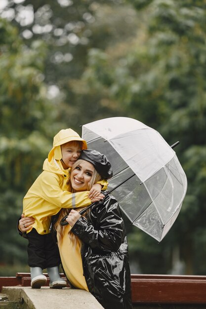 Familia en un parque lluvioso. Niño con impermeables amarillos y mujer con abrigo negro.