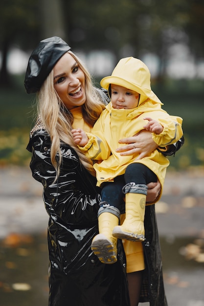 Familia en un parque lluvioso. Niño con impermeables amarillos y mujer con abrigo negro.