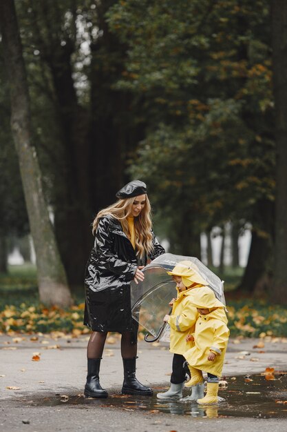 Familia en un parque lluvioso. Niños con impermeables amarillos y mujer con abrigo negro.