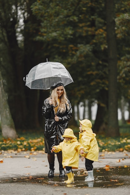 Familia en un parque lluvioso. Niños con impermeables amarillos y mujer con abrigo negro.
