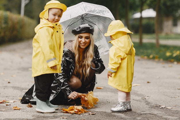 Familia en un parque lluvioso. Niños con impermeables amarillos y mujer con abrigo negro.