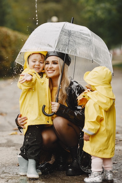 Familia en un parque lluvioso. Niños con impermeables amarillos y mujer con abrigo negro.