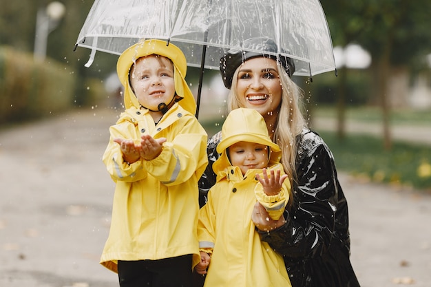 Familia en un parque lluvioso. Niños con impermeables amarillos y mujer con abrigo negro.