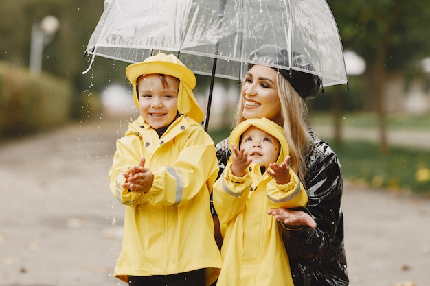 Familia en un parque lluvioso. Niños con impermeables amarillos y mujer con abrigo negro.