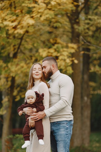 Familia en un parque de otoño. Hombre con un suéter marrón. Niña linda con sus padres.