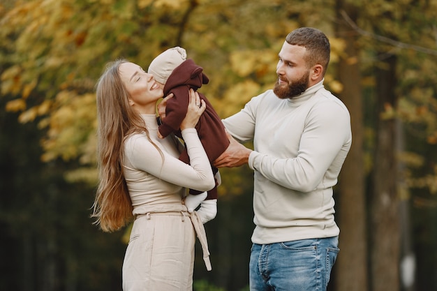 Familia en un parque de otoño. Hombre con un suéter marrón. Niña linda con sus padres.