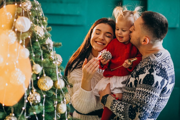 Familia con pequeña hija colgando juguetes en el árbol de Navidad