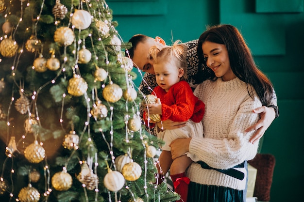 Familia con pequeña hija colgando juguetes en el árbol de Navidad