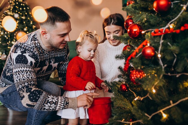 Familia con pequeña hija colgando juguetes en el árbol de Navidad
