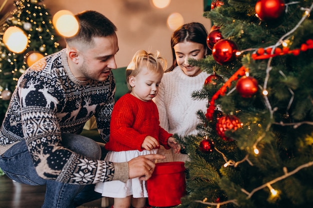 Familia con pequeña hija colgando juguetes en el árbol de Navidad