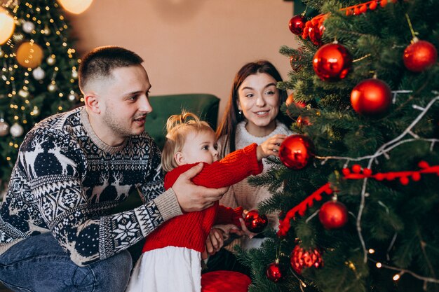 Familia con pequeña hija colgando juguetes en el árbol de Navidad