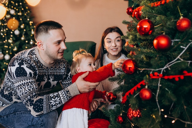 Familia con pequeña hija colgando juguetes en el árbol de Navidad