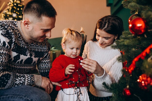 Familia con pequeña hija colgando juguetes en el árbol de Navidad