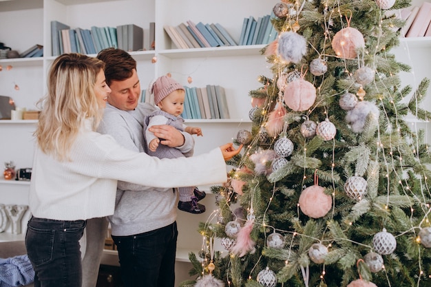 Familia con pequeña hija colgando juguetes en el árbol de Navidad