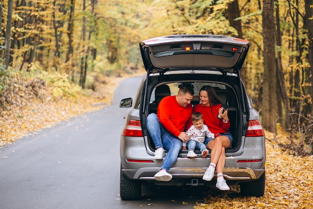 Familia con un pequeño hijo en el parque otoño sentado en el coche