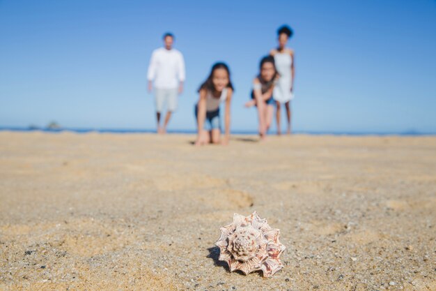 Familia en la playa con concha en primer plano