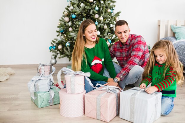 Familia con regalos enfrente de árbol de navidad