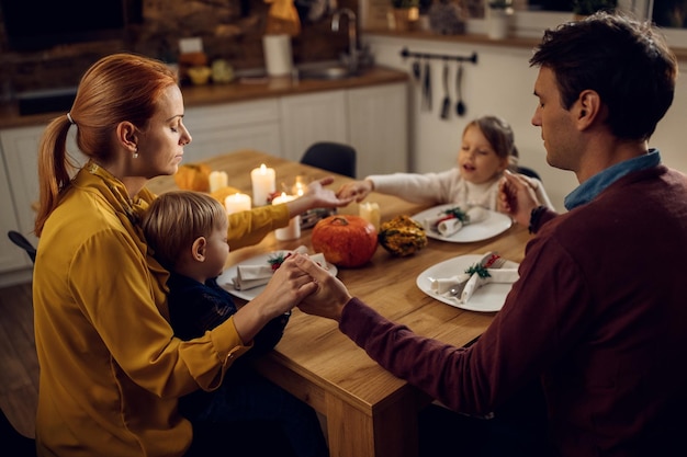 Familia religiosa diciendo gracias antes de la comida de Acción de Gracias en la mesa de comedor