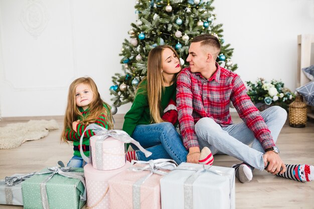 Familia romántica sentados enfrente de árbol de navidad