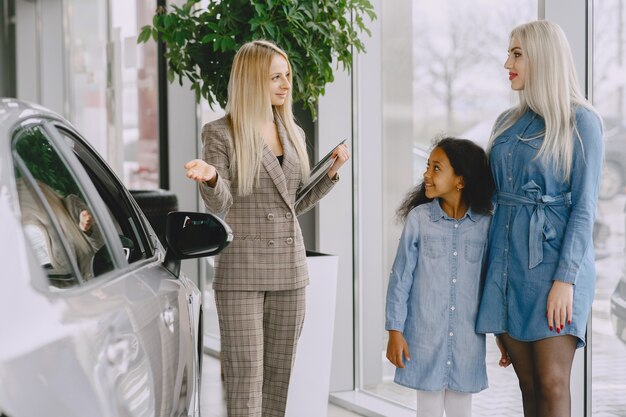 Familia en un salón de autos. Mujer comprando el coche. Niña africana con mther. Gerente con clientes.