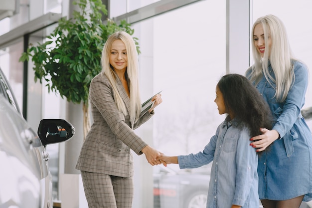 Familia en un salón de autos. Mujer comprando el coche. Niña africana con mther. Gerente con clientes.