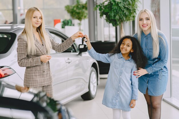 Familia en un salón de autos. Mujer comprando el coche. Niña africana con mther. Gerente con clientes.