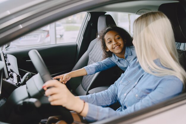 Familia en un salón de autos. Mujer comprando el coche. Niña africana con mther.