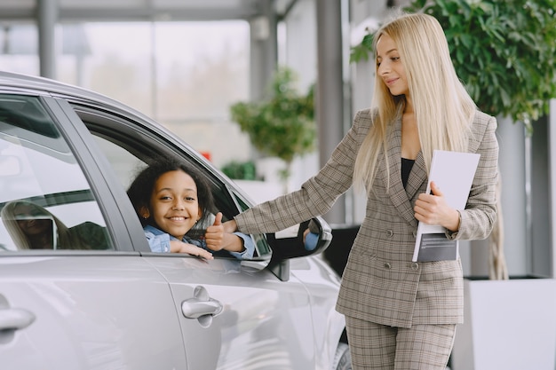 Familia en un salón de autos. Mujer comprando el coche. Niña africana con mther.