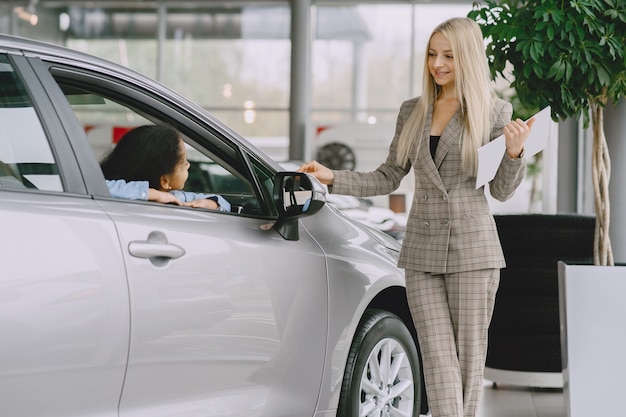 Familia en un salón de autos. Mujer comprando el coche. Niña africana con mther.