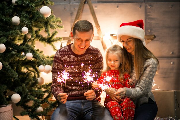 Familia sentada junto al árbol de Navidad con luces de Bengala