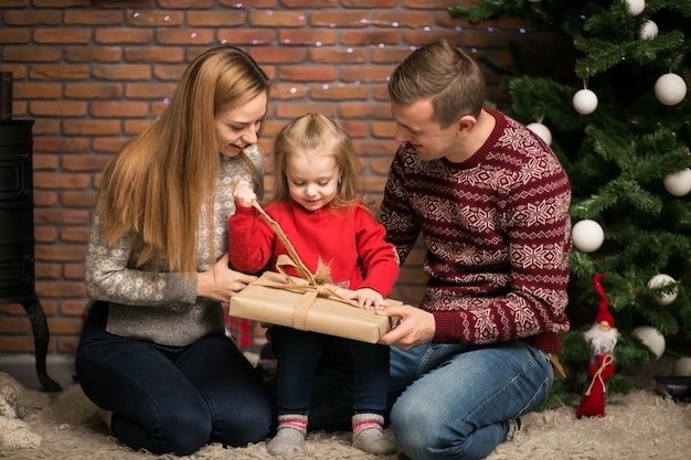 Familia sentada junto al árbol de Navidad con regalos de embalaje de la pequeña hija
