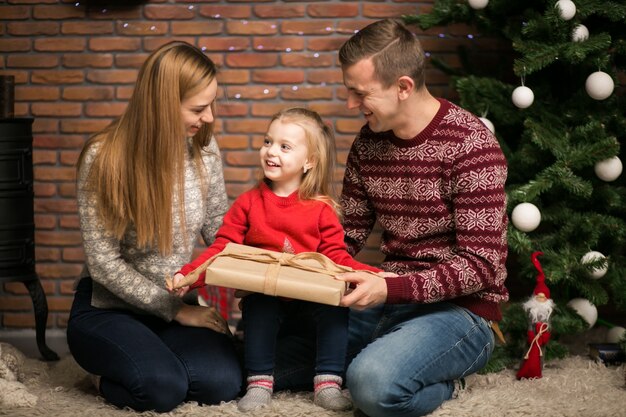 Familia sentada junto al árbol de Navidad con regalos de embalaje de la pequeña hija