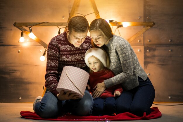 Familia sentada junto al árbol de Navidad con regalos de embalaje de la pequeña hija