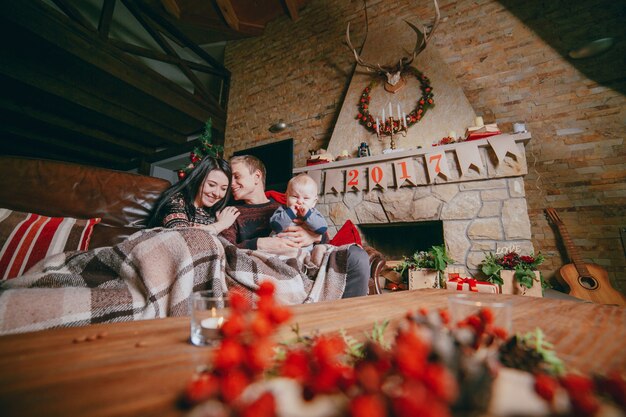 Familia sentada en el sofá arropada con una manta y visto desde los adornos navideños de la mesa de madera